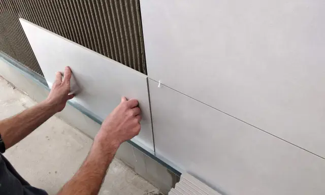 Ręce układają płytki 30x60 na ścianie, tworząc równą, nowoczesną powierzchnię. Widać klej i krzyżyki dystansowe.