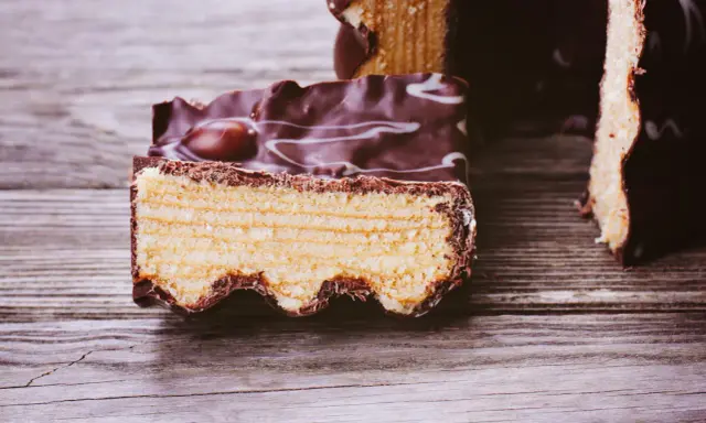 Ein Stück Baumkuchen mit Schokoladenglasur und weißen Zuckerguss-Wirbeln, perfekt für ein Baumkuchen Rezept.