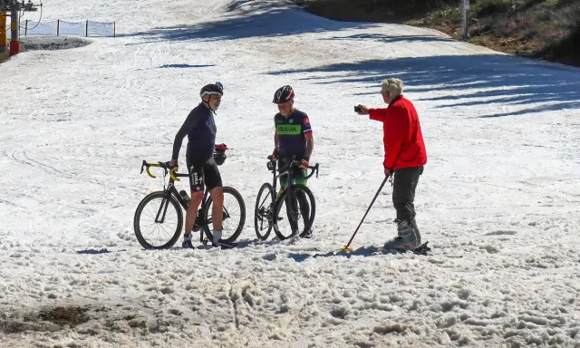 Trzech mężczyzn, dwóch na rowerach, jeden na nartach, dyskutuje na zaśnieżonym stoku. Idealne miejsce, by zapytać, gdzie na narty w marcu.