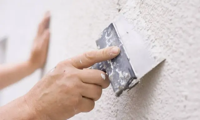 Mano aplicando masa con espátula para reparar gotele en pared.
