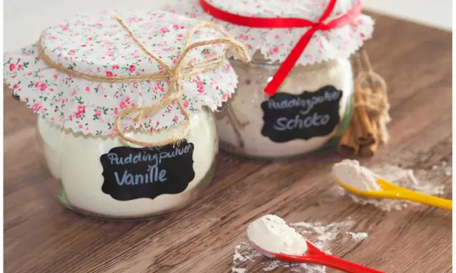 Zwei Gläser mit selbstgemachtem Puddingpulver (Vanille & Schoko) auf einem Holztisch, bereit für köstliche Desserts.