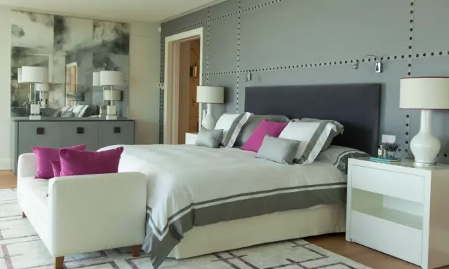 Ideas para diseñar tu habitacion: cama moderna con detalles grises y rosas, mesitas blancas, sofá y espejo decorativo.