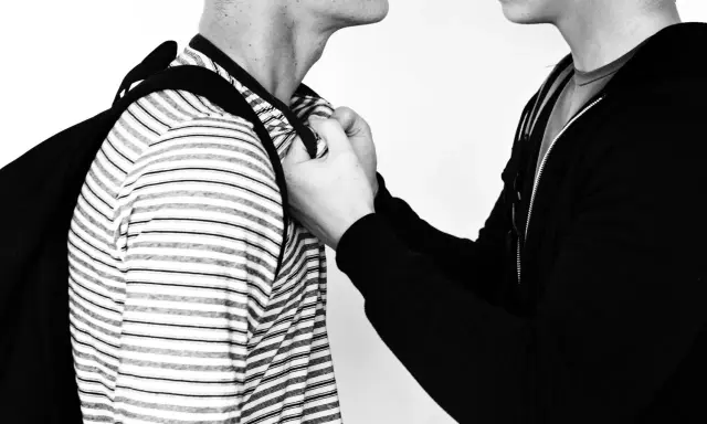 Due persone, una con una felpa nera, afferra l'altra per il colletto. Un'immagine che evoca la psicologia delle persone aggressive.