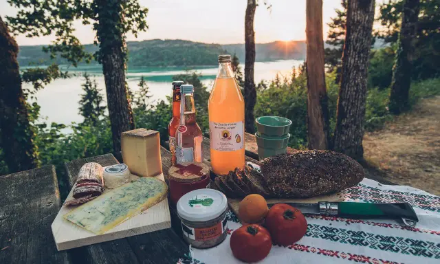 Pique-nique avec fromages, pain de campagne, jus de poire et terrine, un aperçu des spécialités culinaires Jura au bord d'un lac.