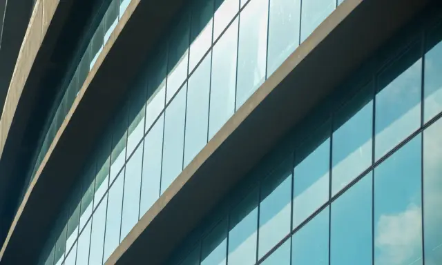 Fachada de edificio moderno con paneles de cristal azul que reflejan el cielo. El **solar glass** captura la luz del sol para generar energía.