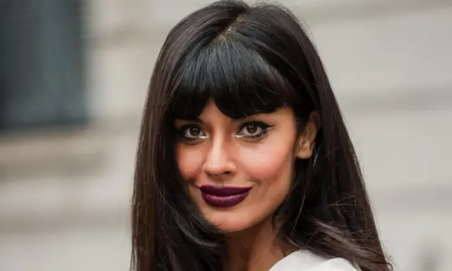 Frau mit leichter Pony und langen, dunklen Haaren, auffälligem Make-up und dunklem Lippenstift.