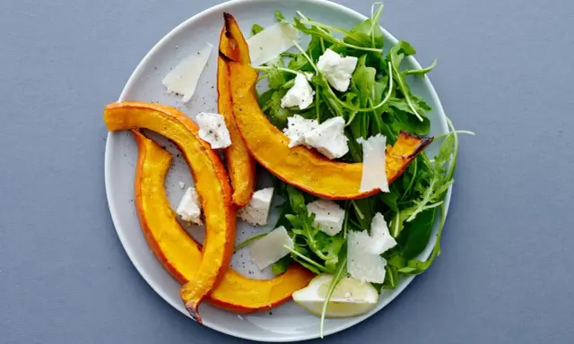 En härlig sallad med ruccola och fetaost, toppad med ugnsrostad pumpa och en citronskiva.