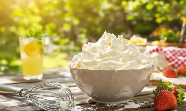 Crème chantilly aérienne et généreuse dans un bol, prête pour un dessert d'été. Une boisson fraîche et des fraises complètent ce tableau gourmand.
