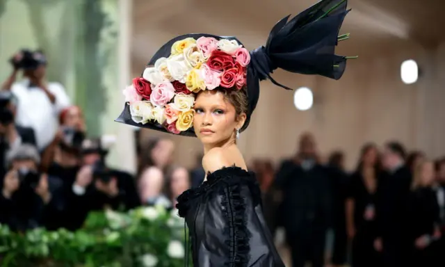 Zendaya stuns at the Met Gala in a dramatic black gown and a voluminous hat adorned with a cascade of colorful roses.