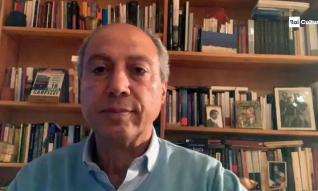 Carmine Abate, con libreria alle spalle, parla in videochiamata.