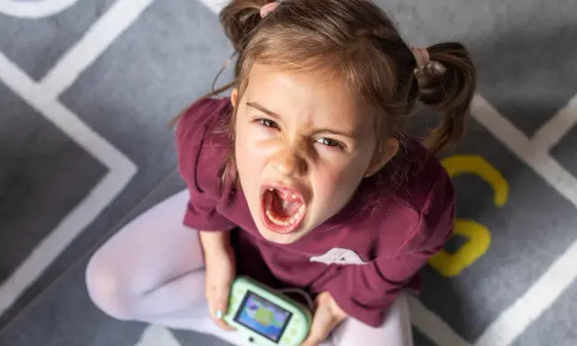 Niña con expresión de enfado y consola de videojuegos, un ejemplo de comportamiento disruptivo significado.