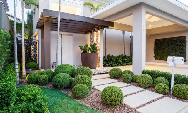 Vialetti giardino moderni con siepi sferiche e un pergolato in legno creano un percorso accogliente verso la casa.