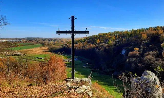 Czarny krzyż na skale góruje nad jesienną doliną Grzybowską. W oddali widać pola i lasy w barwach złota i czerwieni.