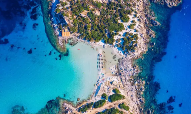Spiaggia paradisiaca con acque cristalline, perfetta per itinerari Sardegna nord 7 giorni. Ombrelloni e lettini invitano al relax.
