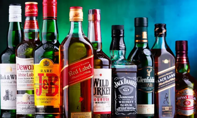 Eine Reihe von Whiskyflaschen, darunter Johnnie Walker Red Label, Jack Daniel's und Chivas Regal. Die Frage "wie viel prozent hat whisky" wird durch die 40% Vol. auf der Jack Daniel's Flasche beantwortet.