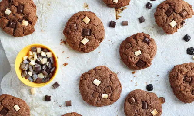 Gros plan sur des cookies au chocolat parsemés de morceaux de chocolat blanc et noir. Un petit bol jaune contient des morceaux de chocolat, comme un cookie stick.