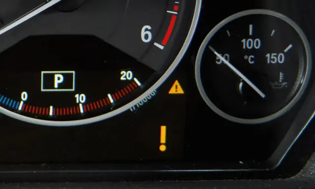 Na desce rozdzielczej świeci żółty trójkąt z wykrzyknikiem, sygnalizując problem. Obok wskaźnik temperatury silnika.