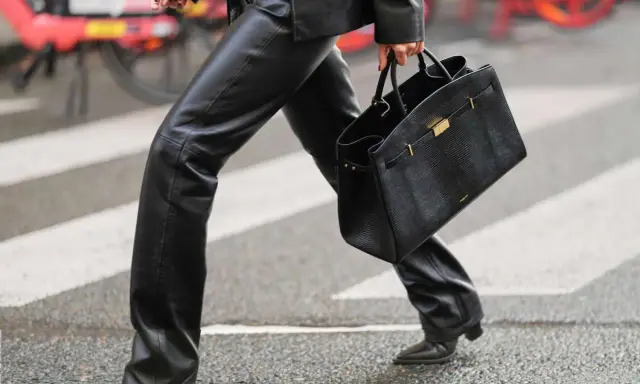 A person walks across a crosswalk in a chic leather pants outfit, perfect for winter. They carry a stylish black handbag.
