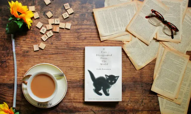 Libro "If Cats Disappeared From The World" con un gattino nero, occhiali, fiori e una tazza di tè. La trama esplora un mondo senza gatti.