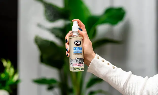 Dłoń trzyma butelkę K2 SKIRON ODOR REMOVAL, która rozpyla mgiełkę, by zlikwidować nieprzyjemny zapach w pokoju po nocy.