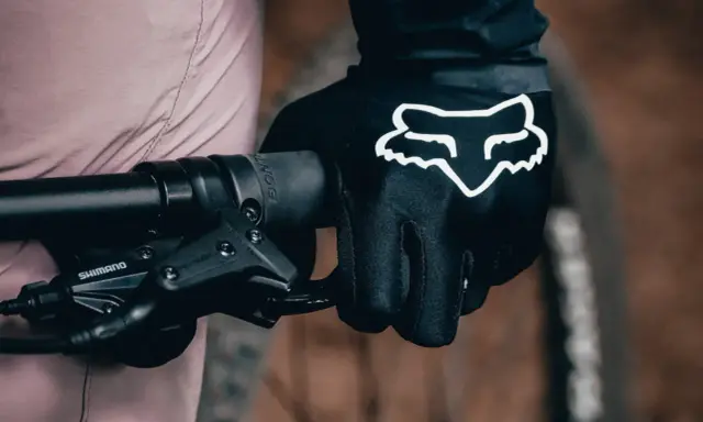 Dłoń w czarnej rękawiczce Fox z białym logo, gotowa do jazdy. Idealne rękawiczki na rower dla każdego miłośnika dwóch kółek.