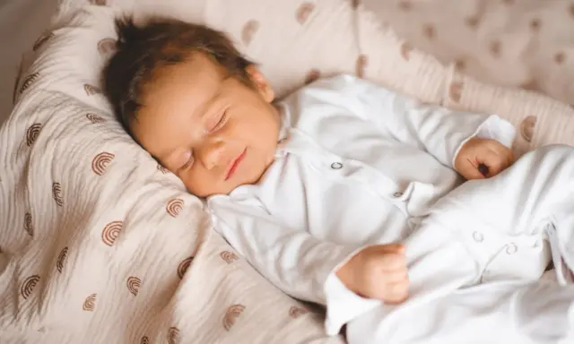 Un neonato dorme sereno, avvolto in una copertina con arcobaleni. Un dolce sogno per questi bambini piccoli.