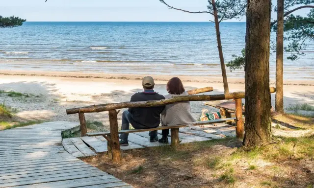 Para relaksująca para siedzi na ławce, patrząc na morze. Idealne miejsce na sanatoria nad morzem.