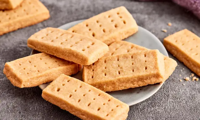 Goldbraune Shortbread-Kekse, perfekt für ein einfaches Shortbread Rezept. Sie liegen auf einem Teller und daneben ein lila Tuch.