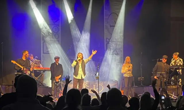 Medlemmar av Dr Hook uppträder på scenen under en konsert, med sångaren i centrum som sjunger i mikrofonen.