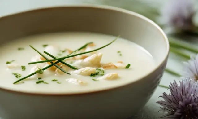 Un bol de velouté d'asperges crémeux, garni de pointes d'asperges, de ciboulette ciselée et de quelques éclats croustillants.