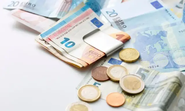 Euro banknoty i monety, czyli waluta w Grecji. Widać banknot 10 euro w metalowym klipsie, a obok monety i banknoty 5, 20 euro.