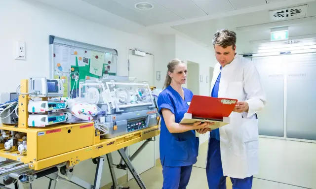 Personale medico discute in terapia intensiva neonatale accanto a un'incubatrice.