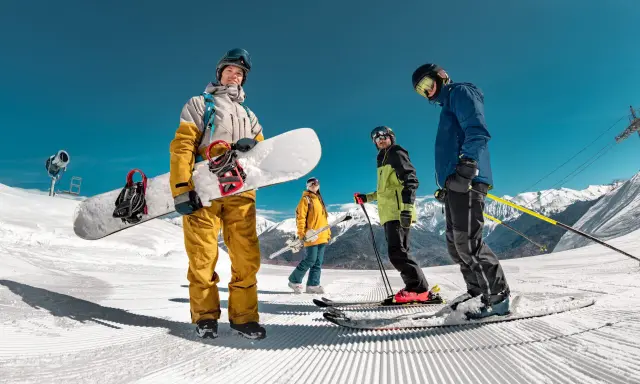 Grupa narciarzy i snowboardzistów na ośnieżonym stoku z widokiem na góry.
