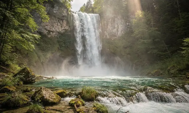 Cascata maestosa nei Laghi di Plitvice, con acqua turchese e rocce muschiose. La luce solare filtra tra gli alberi, creando un'atmosfera magica.