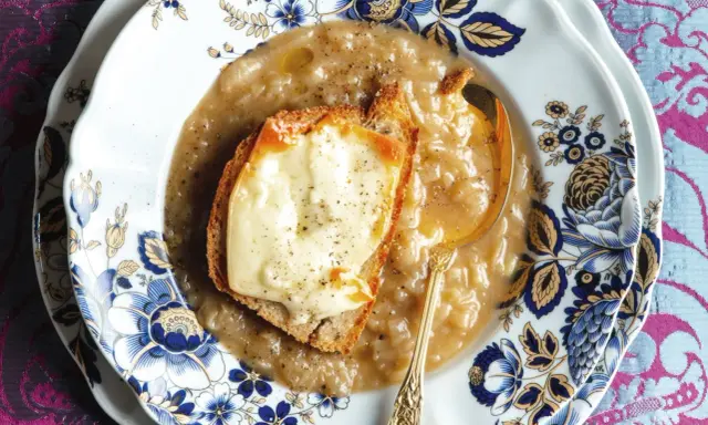 Piatto di zuppa di cipolle fumante, con crostino di pane e formaggio fuso, servita su un elegante piatto decorato.