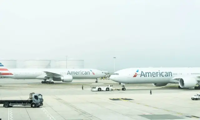 Dwa samoloty American Airlines na płycie lotniska, gotowe do przyjęcia bagażu rejestrowanego.