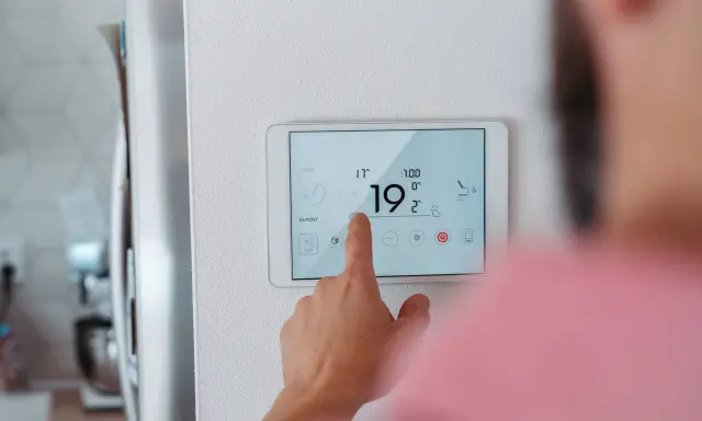 Main d'une personne ajustant la température sur un écran tactile, optimisant la programmation chauffage pour un confort idéal.