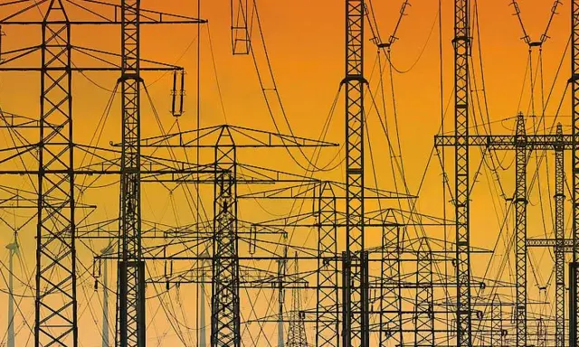 Silhouetten von Strommasten und Leitungen vor einem orangen Himmel. Ein Netz von **Polen Strom** erstreckt sich in die Ferne.