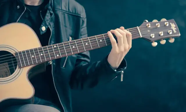 Mężczyzna w skórzanej kurtce gra na gitarze. Akordy układają się w piękną tonację d dur, tworząc melodyjną opowieść.