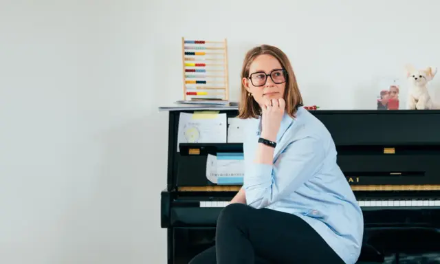 Annelien de Dijk, met een blik vol vrijheid, zit bij een piano, omringd door muziek en een telraam.