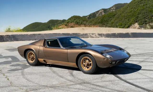 Ein brauner Lamborghini Miura S steht auf einer asphaltierten Straße mit Bergkulisse.