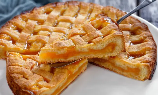 Una fetta di crostata senza glutine con ripieno di albicocche dorate, la sua pasta friabile e la griglia decorativa invitano a un assaggio goloso.