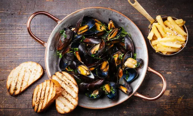 Moules marinières, une spécialité culinaire normande, servies dans une marmite en cuivre avec des frites et du pain grillé.