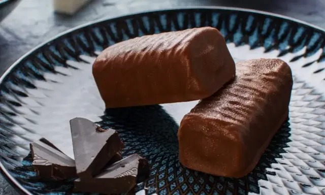 Dwa czekoladowe batony proteinowe na talerzu, obok kawałki gorzkiej czekolady. Idealne do domowego batony proteinowe przepis.