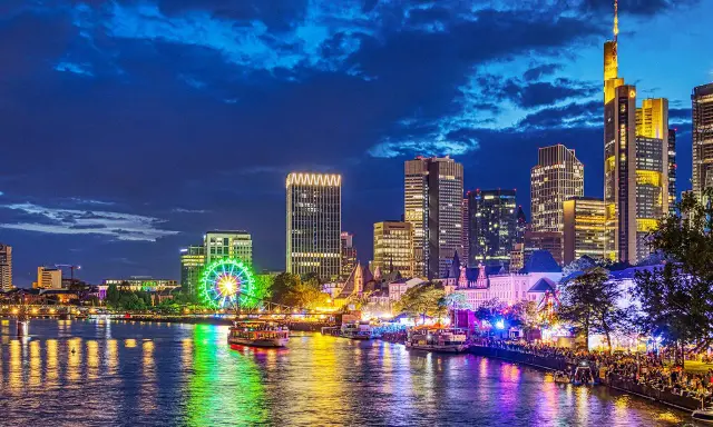 Frankfurt Mainufer bei Nacht: Lichtermeer, beleuchtetes Riesenrad und Skyline spiegeln sich im Wasser.