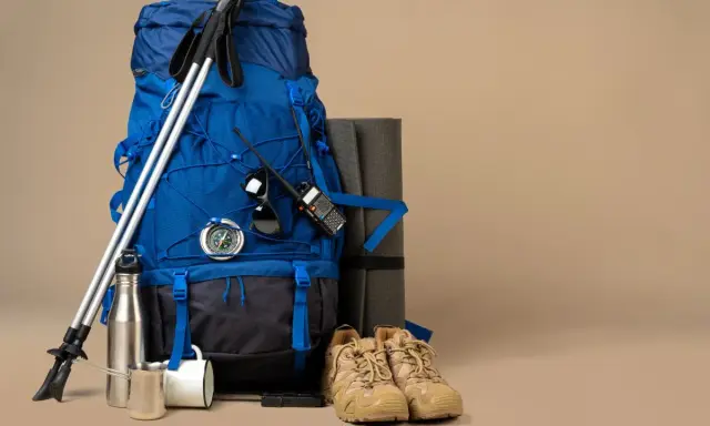 Niebieski plecak trekkingowy, kije, buty, mata, kompas, krótkofalówka i termos – wszystko gotowe na wyprawę.