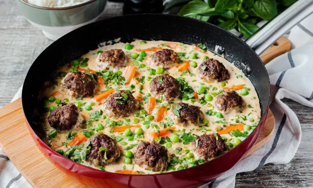 Herzhafte Fleischbällchen in cremiger Sauce mit Erbsen und Karotten, ein köstliches Wikingertopf Rezept, serviert in einer roten Pfanne.
