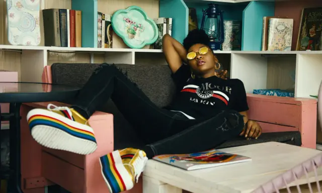 Une jeune femme aux lunettes rondes dorées se détend sur un canapé, ses chaussures arc-en-ciel colorées bien en évidence. Elle incarne le parfait "chill traduction".