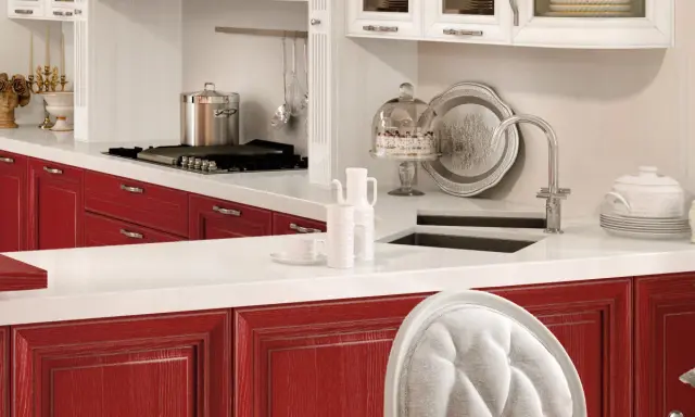 Cucina con ante rosse, piano bianco, pentola sul fornello, torta sotto campana di vetro. Okite cos'è? Un piano di lavoro resistente e bello.