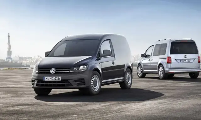 Dos furgonetas Volkswagen Caddy, una negra y otra plateada, demuestran su versatilidad como vehículo mixto adaptable en un entorno portuario.